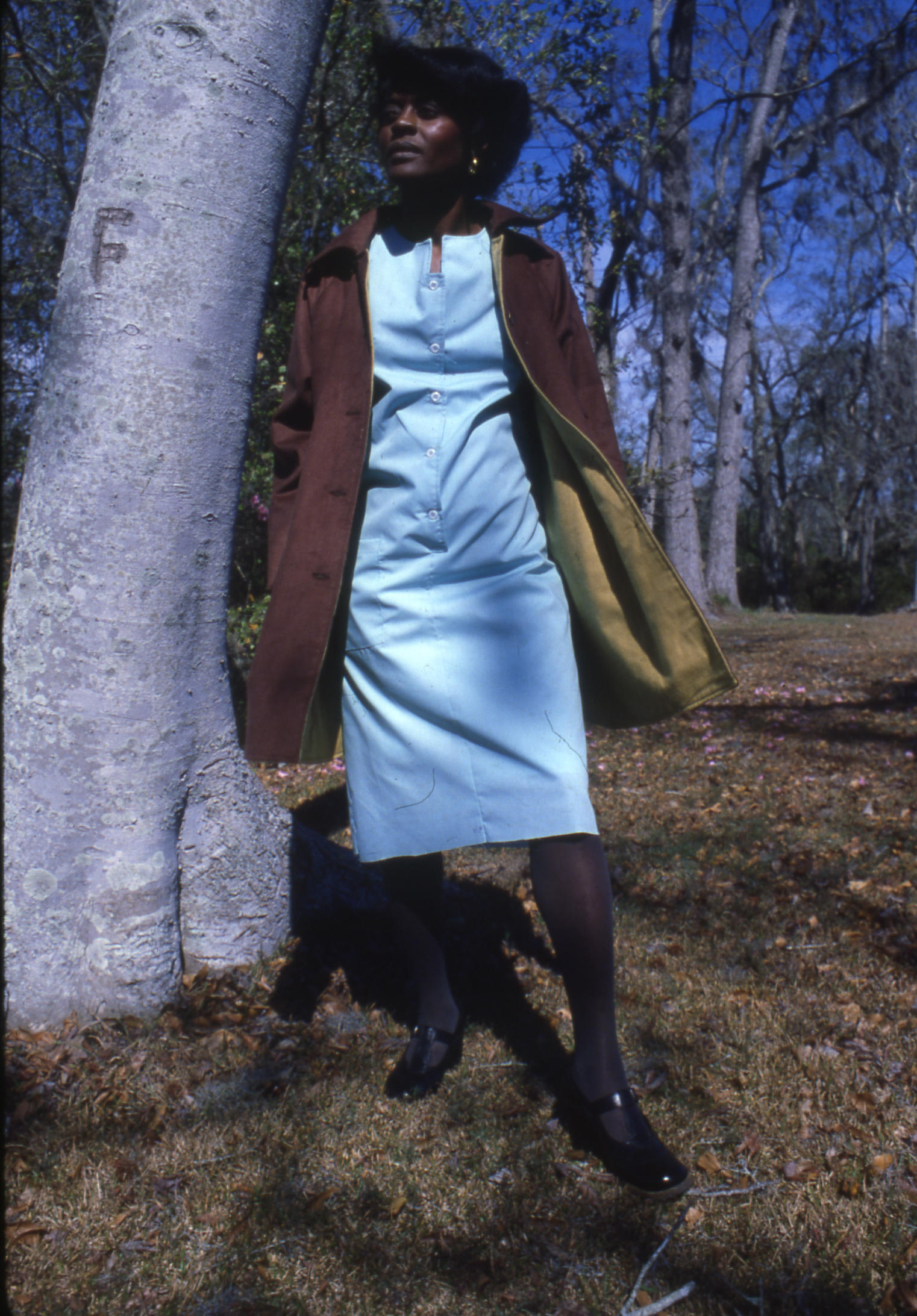 Slide 10: An image of a Black woman striking a pose. She is outside and wearing a blue, mid-length dress (which was a prison uniform for women), a brown jacket, and black shoes.
