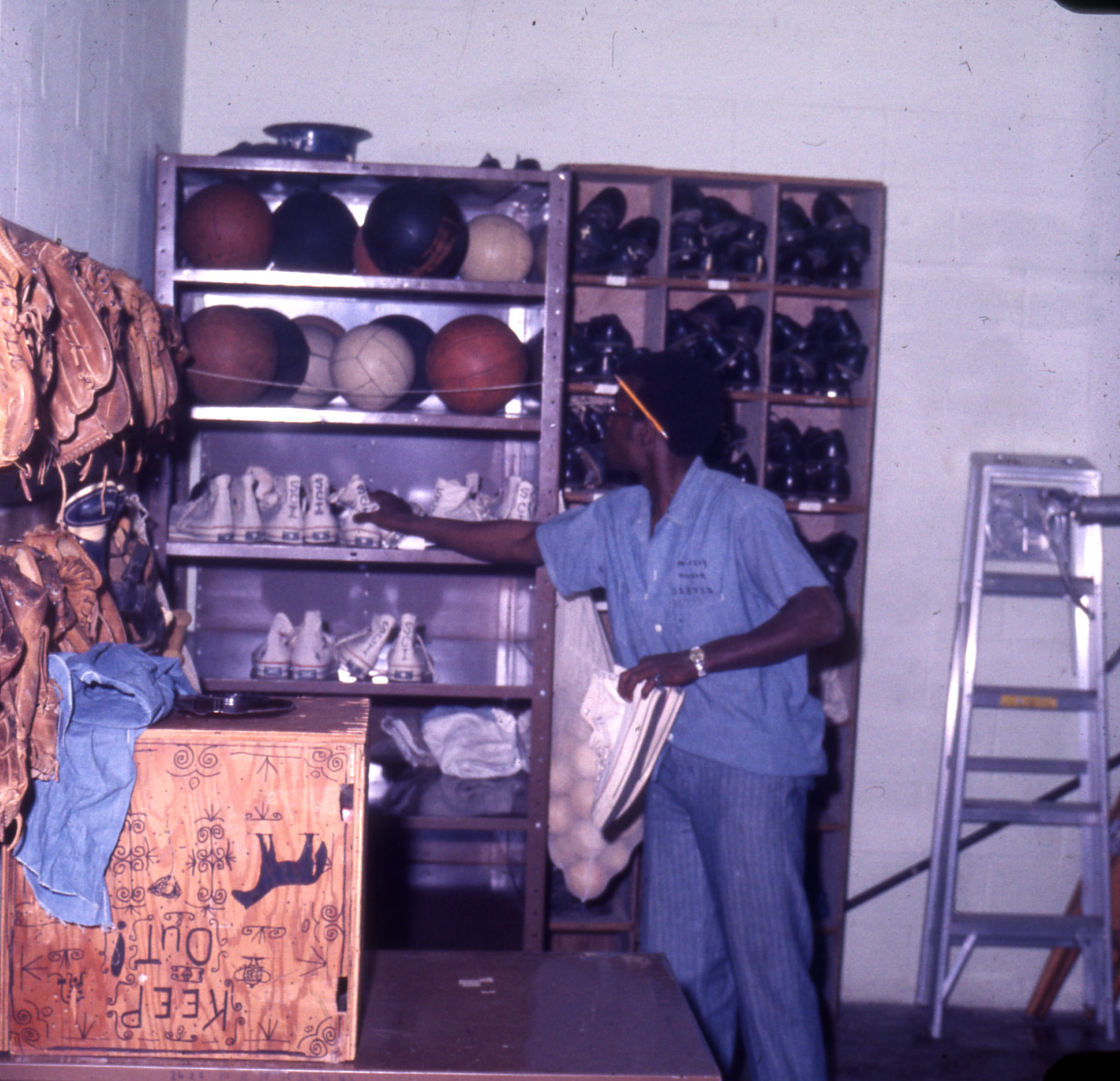 Slide 8: This is a photo of a Black man in a blue prison uniform. He appears to be working in an equipment room, and is surrounded by shelves of basketballs, sneakers, volleyballs, and baseball gloves.