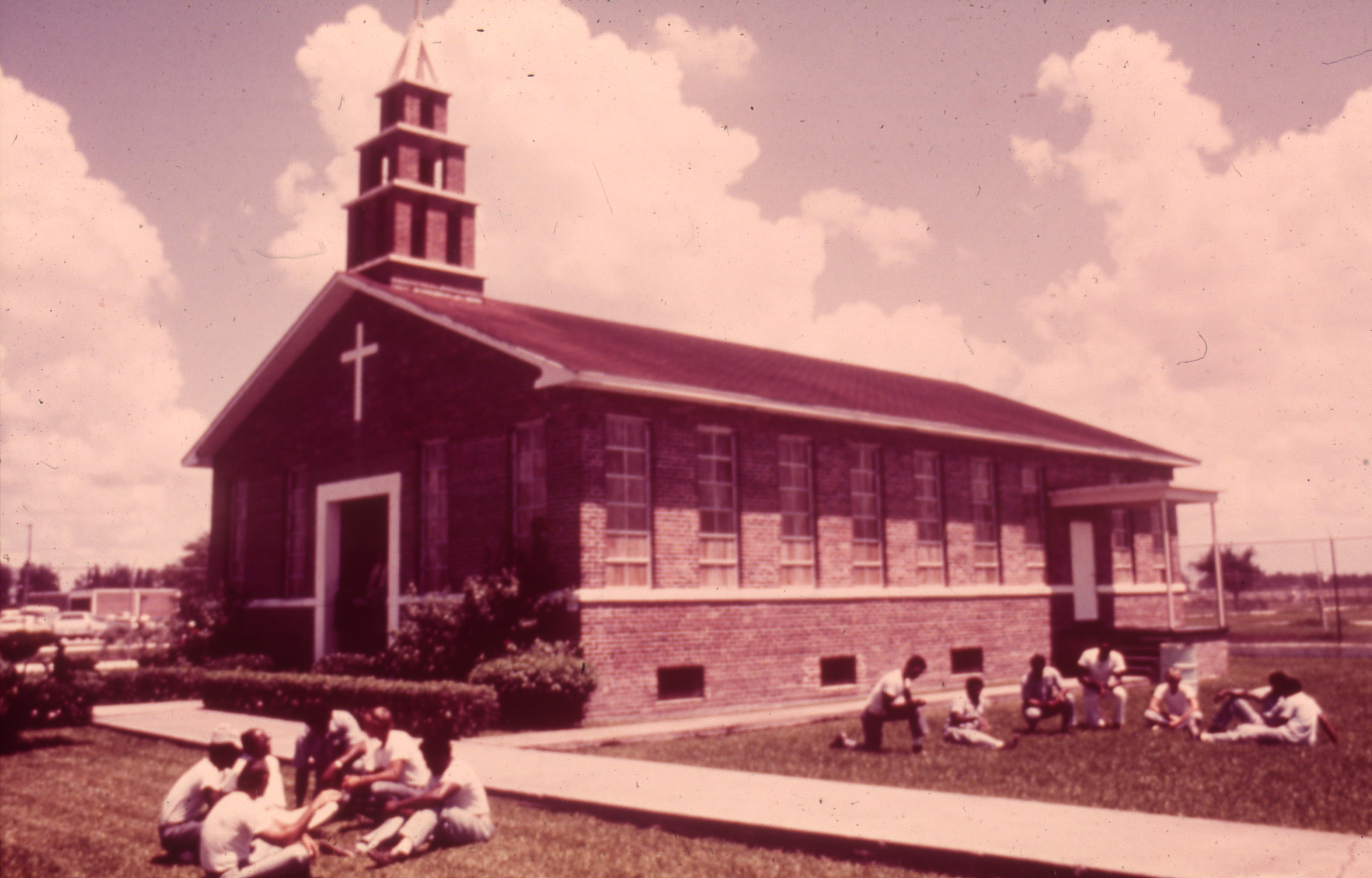 Slide 16: A photo of a chapel, with men sitting in small groups outside in the grass.