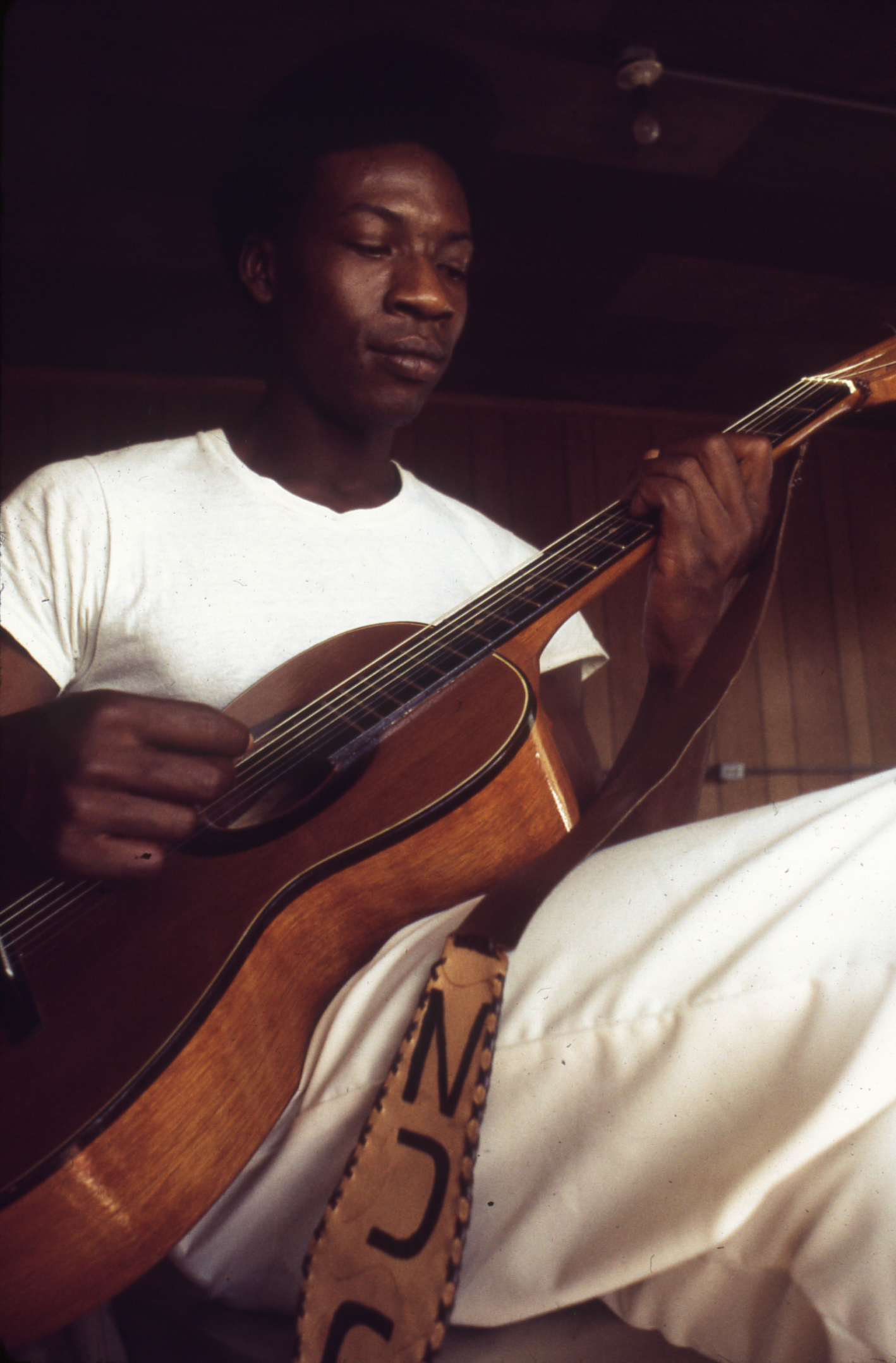 Slide 9: This is a closeup picture of a Black man in a white prison uniform playing a nylon string guitar.